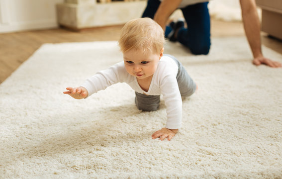 Determination. Pretty little determined child feeling glad while being at home with a kind loving father and crawling on the floor