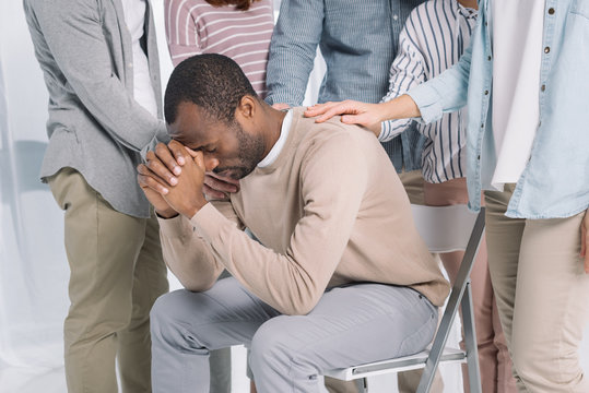cropped shot of people supporting depressed middle aged african american man during group therapy
