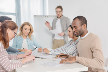 Obraz premium multiethnic team working with papers together while man standing near whiteboard behind