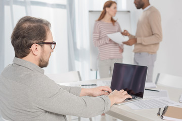 middle aged man in in eyeglasses using laptop with blank screen in office