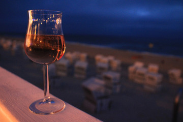 Rosé Weinglas auf Brüstung in der Abenddämmerung mit Strand und Meer verschwommen im Hintergrund.Where: Westerland, Sylt.When: 20.07.2013.