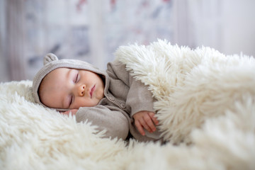 Sweet baby boy in bear overall, sleeping in bed with teddy bear