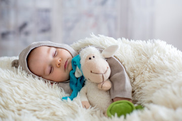 Sweet baby boy in bear overall, sleeping in bed with teddy bear