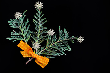 Branches of green juniper with a yellow bow made of fabric and white plastic snowflakes in the form of a bouquet on black background abstract