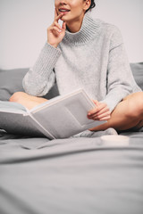Girl sitting on bed and reading book in the morning