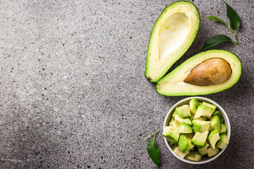 Chopped avocado in a bowl and halves on concrete background. Top view, copy space.