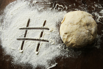 Hashtag written in flour and raw ball of dough. Number sign on floured wooden surface and fresh...