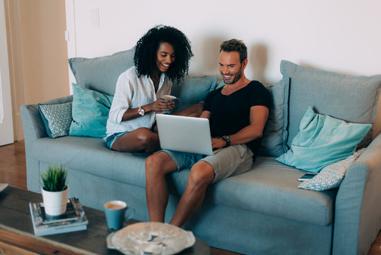 Happy Young Couple Relaxed At Home In The Couch On The Mobile Phone And Computer