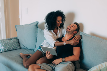 Happy young couple relaxed at home sitting in the couch on the tablet