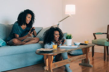 Happy young two black women sitting in the couch playing video games  .