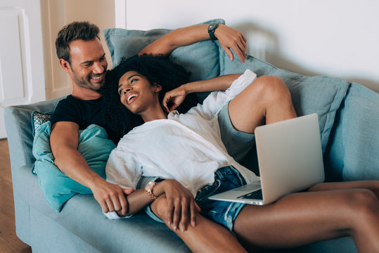 Happy young couple relaxed at home lying down in the couch on the computer