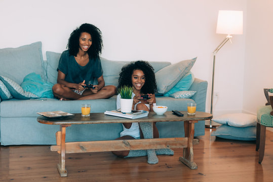 Happy Young Two Black Women Sitting In The Couch Playing Video Games  .