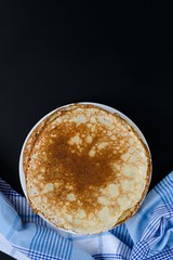 Russian pancakes with checker napkin on black background.