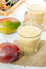 Fresh mango smoothie in a glass over white table.
