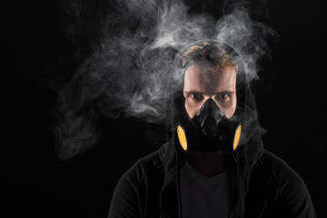 Man in black hood wearing protective filter mask surrounded by clouds of smoke