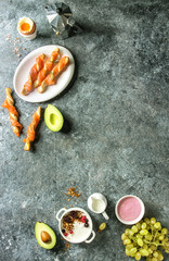 Breakfast set with smoked salmon on crispy breadsticks, yogurt, smoothie, avocado, muesli, milk, berries and green grape over blue texture background. Top view, copy space. Food background