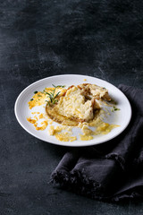 Traditional french onion soup with cheese and bread served in white ceramic plate with rosemary and textile napkin over black texture background.