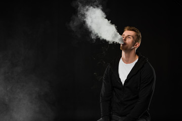 Young bearded man vaping electronic cigarette surrounded by clouds of steam