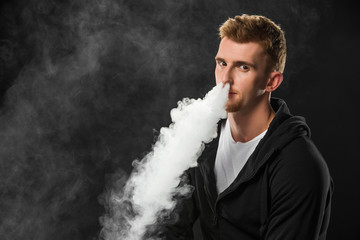 Fototapeta na wymiar Young bearded man exhaling smoke of electronic cigarette surrounded by clouds of steam