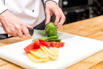 cropped image of chef cutting colored bell peppers