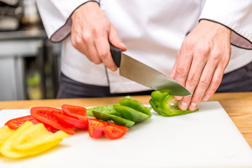 cropped image of chef cutting colored bell peppers