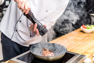 cropped image of chef seasoning frying meat with pepper