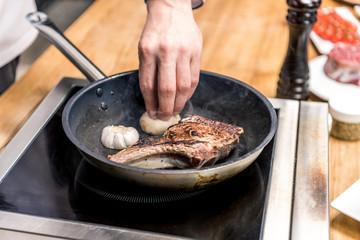 cropped image of chef putting garlic to frying meat