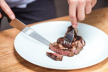 cropped image of chef cutting fried meat with knife and fork