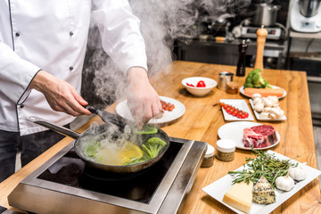 cropped image of chef frying yellow and green bell peppers with broccoli