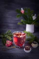 Fruit and hibiscus tea in transparent cup, luxury chocolates candy and christmas tree branch on a dark background