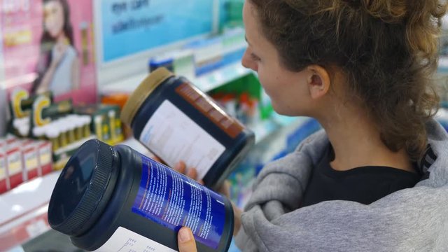 Woman Choosing Protein Powder Supplement In Drugstore. Bodybuilding Sport Diet. Closeup. 4K. 