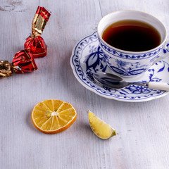 A porcelain cup with black tea. Dried citrus fruits. Chocolate candies. On a light wooden background.