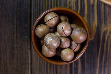 Top view of macadamia nuts in brown ceramic bowl on wooden table.