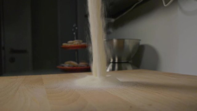 Flour is poured onto a wooden board on a kitchen counter - closeup - slow motion