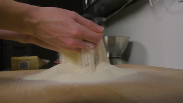 A woman takes a handful of flour off a wooden board on a kitchen counter and lets it fall - closeup - slow motion