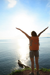 Young woman with raised hands standing at seaside mountain