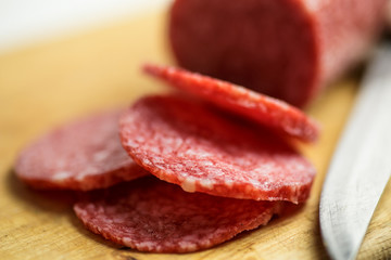 Salami on wooden cutting board with knife, macro photo with selective focus. Slices of sausage