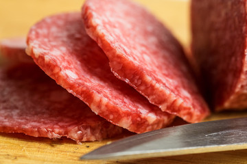 Salami on wooden cutting board with knife, macro photo with selective focus. Slices of sausage