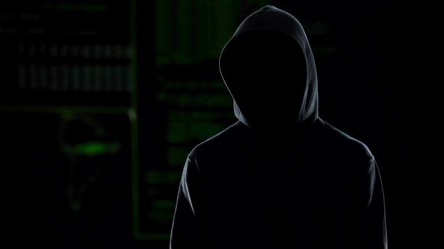 Unknown hooded male hacker looking into camera, global cybercrime problem