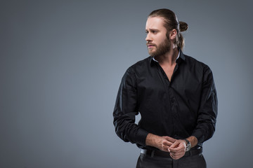 Handsome bearded man in black shirt looking away, isolated on gray