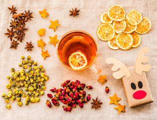 ecological deer craft from recycled paper on linen background with cup of hot tea, lemons, oranges,flowers and decorations