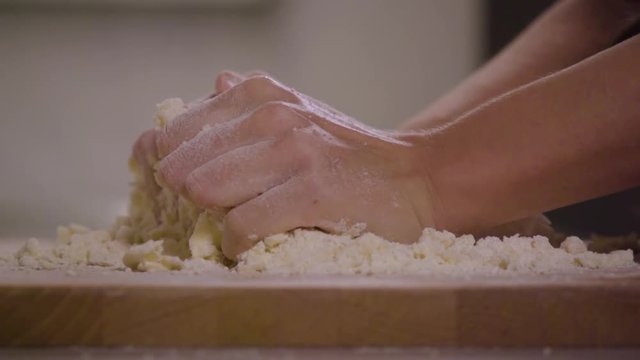 A woman kneads crumbly pastry dough on a kitchen counter - closeup - slow motion