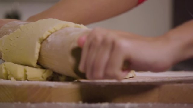 A woman rolls out dough with a rolling pin on a kitchen counter - closeup - slow motion