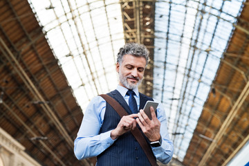 Mature businessman with smartphone on a train station.