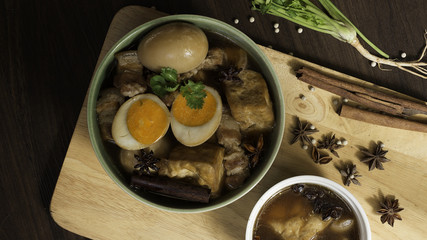 Stewed eggs in a bowl and putting green on a wooden tray. Within half an egg red. Coriander spices and set aside. On black background.
