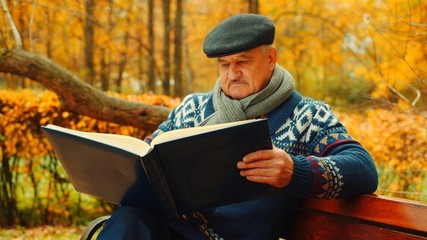 Senior with big memory photo album on the bench in the autumn park