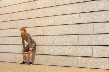 Male jogger resting after morning run while standing against wall background with copy space area for your text message or advertising, young fit men taking break between training outdoors