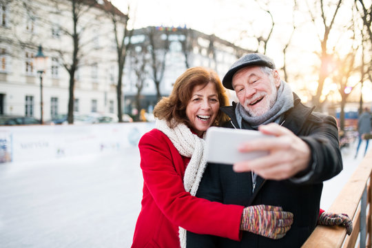 Senior couple with smartphone on a walk in a city in winter.