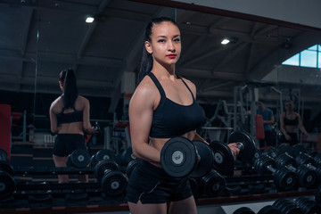 Fototapeta na wymiar Muscular girl posing with dumbbells in the gym