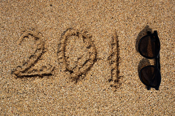 Fototapeta na wymiar Text 2018 on sand with sunglasses. Concept of new year holiday